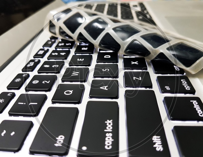 Silicon laptop keyboard cover raised with a hand to show underlying laptop isolated keys