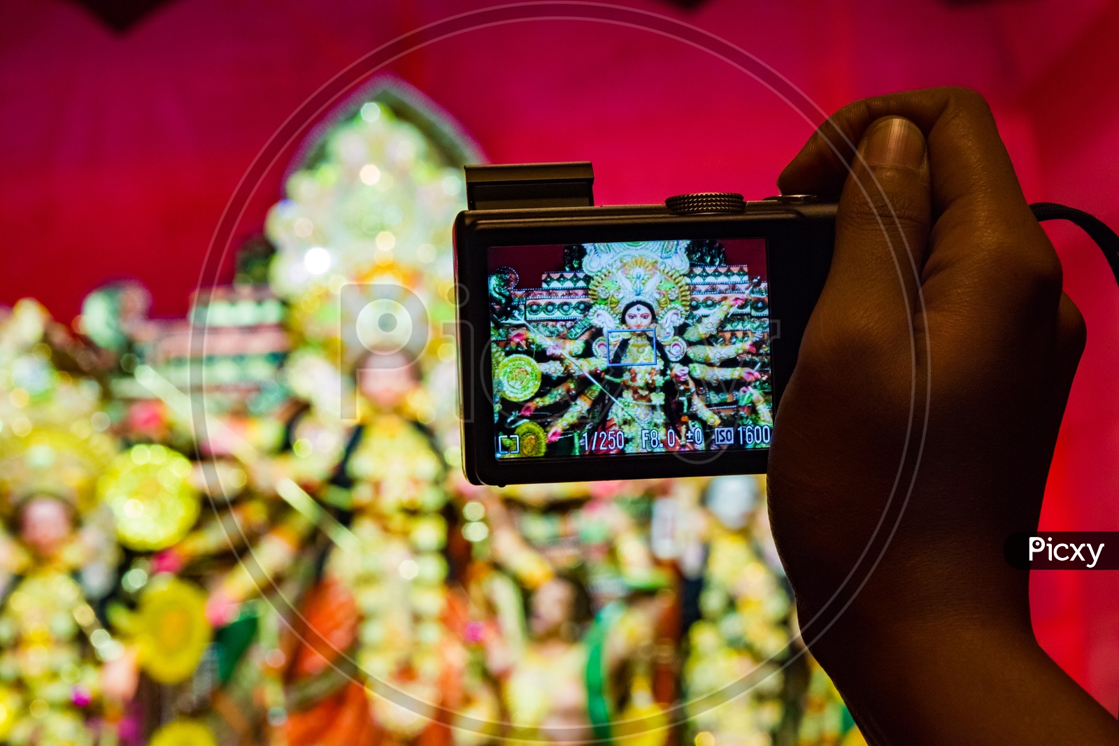 Camera In Hand Taking Photo Of Durga Idol In Background Shallow Depth Of Field