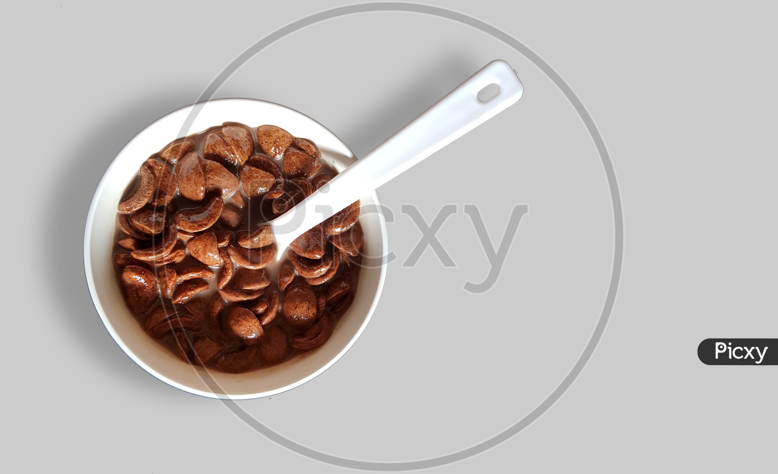 Chocolate Cornflakes Dipped In Chocolate Milk In A White Bowl In Light Background With Spoon