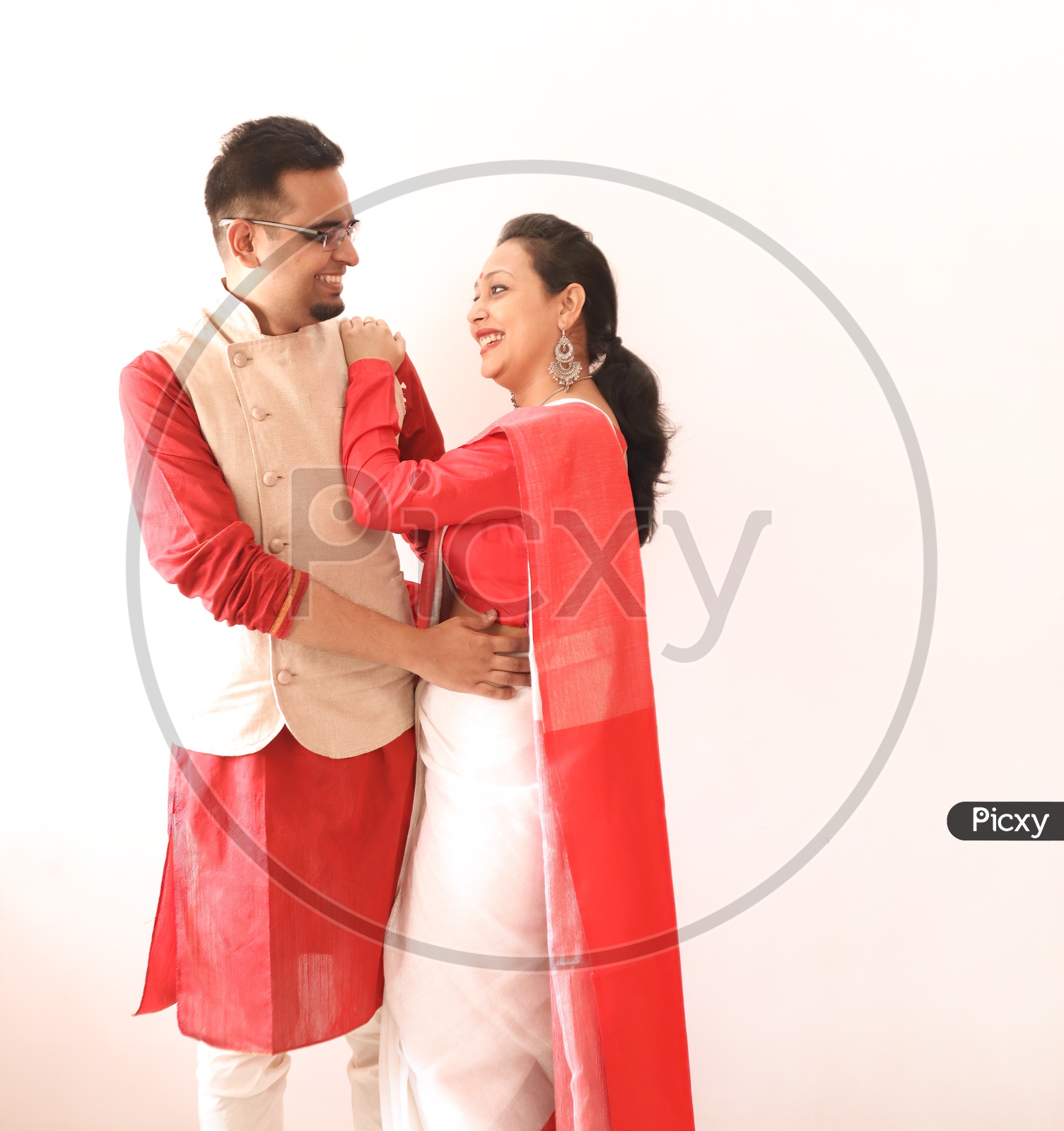 A Young Indian Bengali Assamese Married Romantic Couple Dressed In Red And White Ethnic Indian Dress, Looking At Each Other And Smiling
