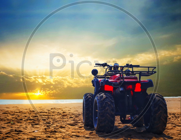 Four Wheeler Dirt Bike On Sand Of Sea Beach During Sunrise With Dramatic Colourful Sky