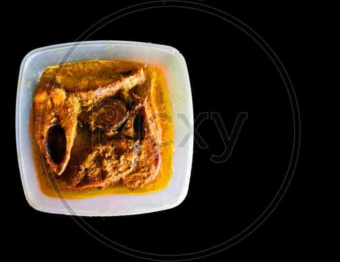 An Indian Cuisine Fish Mustard Curry In A Plasic Container In Black Background
