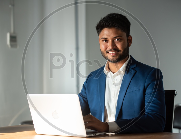 Happy Young Indian Businessman With Smile face Working on Laptop At Office Work Space Background