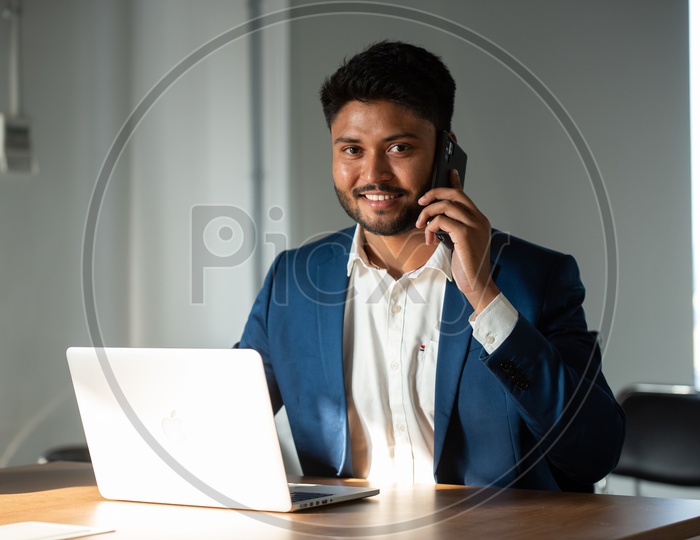 Indian Businessman Speaking In Smartphone At Office Work space Background