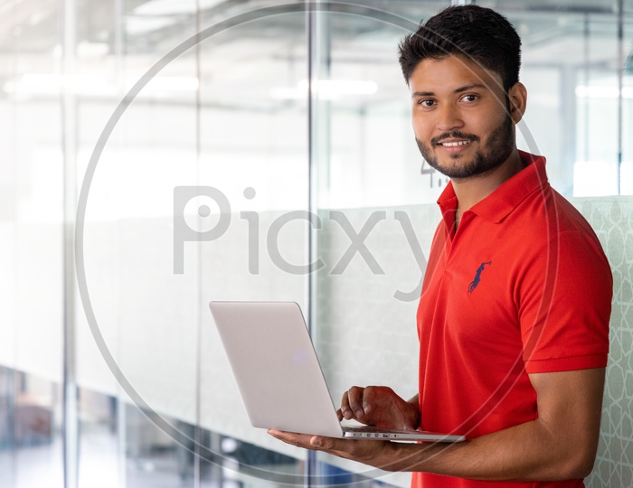 Indian Male Student Holding  a Laptop With Indoor Backdrop