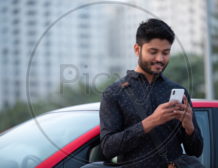 Young Indian Man Using Smartphone by Leaning To a Car