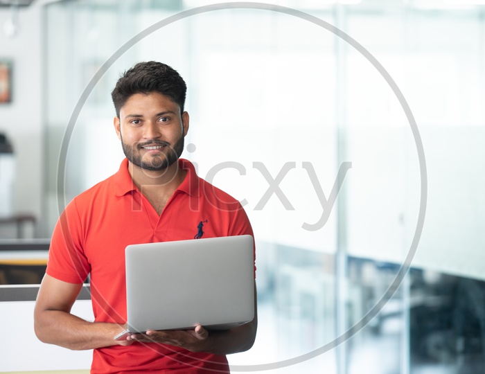 Indian Happy Male Student Holding Laptop In Indoor Background