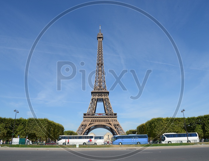 Eiffel Tower With Tourists Buses Parked And With Blue Sky Background