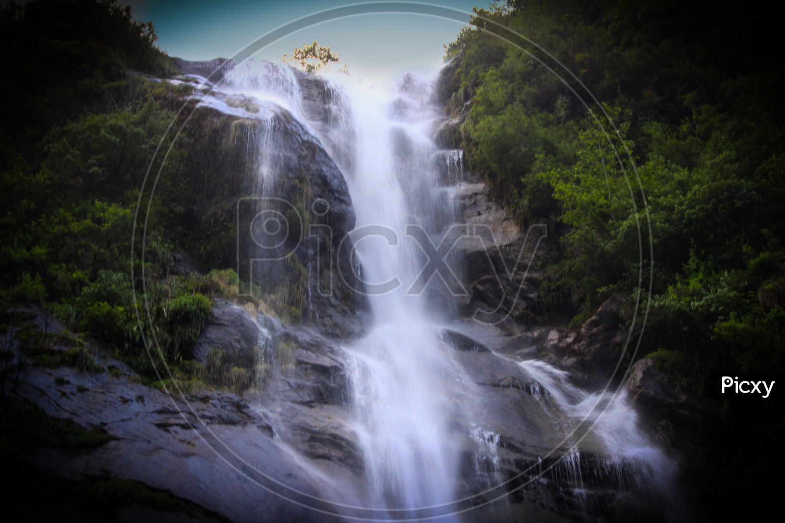 A Natural Waterfall In Hills Of Sikkim, India In Between Forest Vegetation With Captured With Slow Shutter Speed
