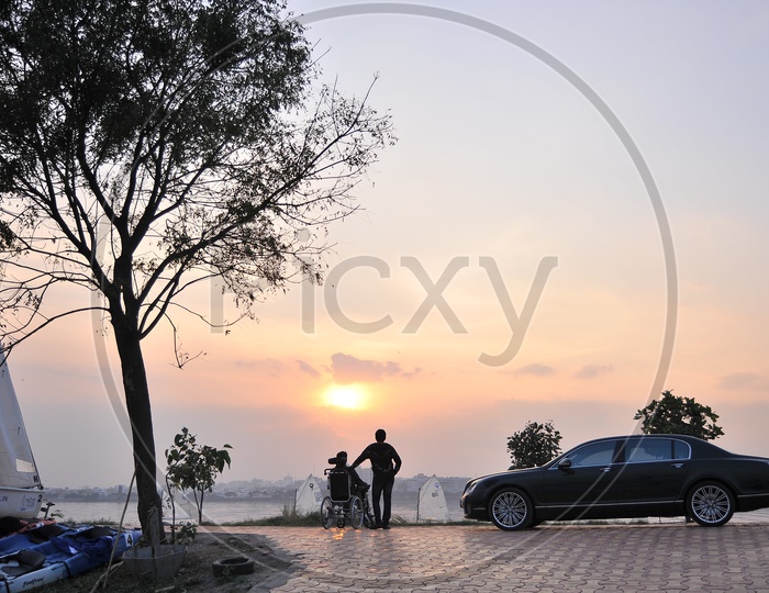 Silhouette Of Man And Handicapped man enjoying Sunset Over a Water Front