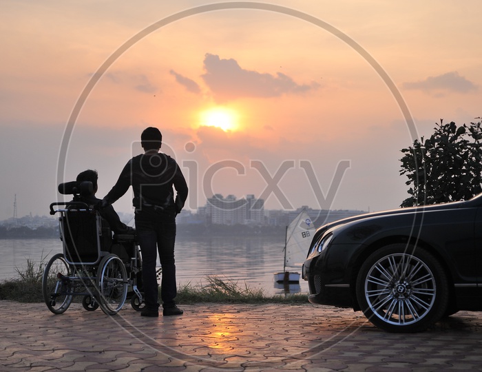 Silhouette Of Man And Handicapped man enjoying Sunset Over a Water Front
