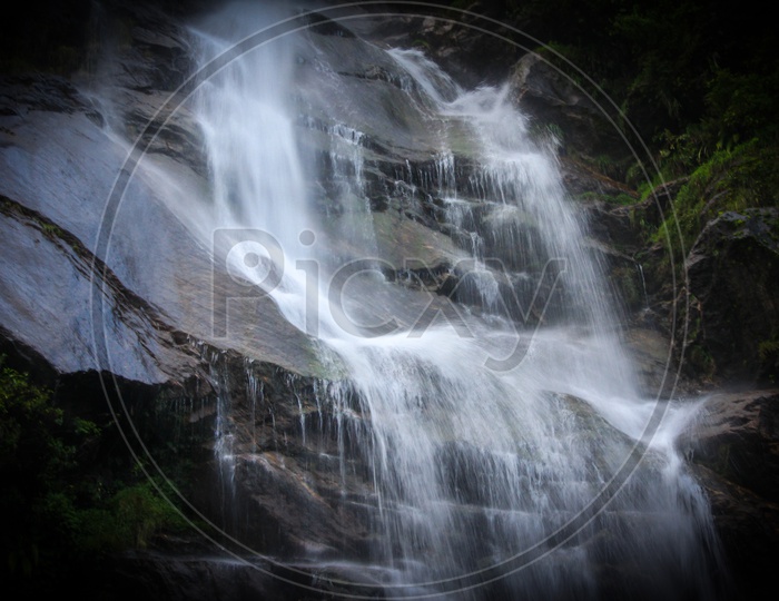 A Natural Waterfall In Hills Of Sikkim, India In Between Forest Vegetation With Captured With Slow Shutter Speed