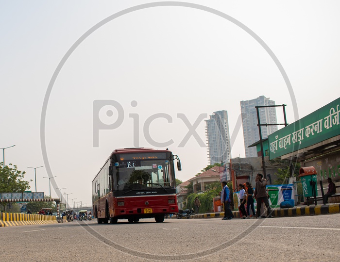 DTC AC red color bus at a bus stop and passengers waiting to get into the bus