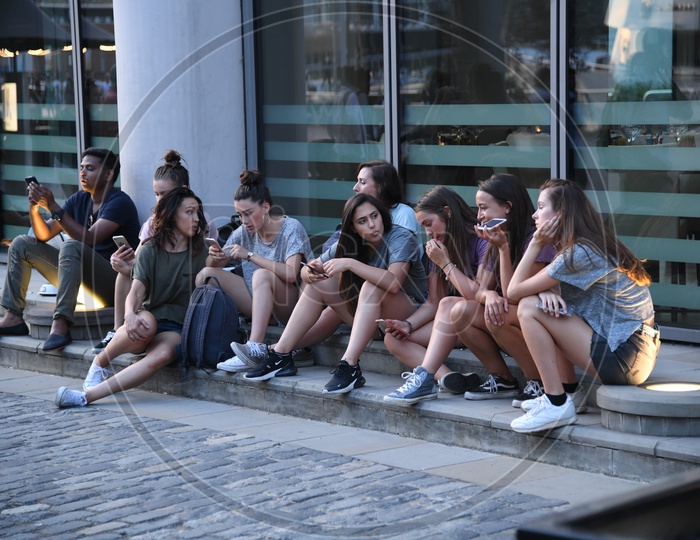 Young Woman Sitting As a Group And Checking Their Smartphones on Streets Of London