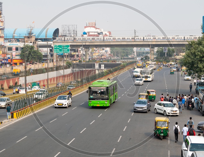 Blue line of Delhi metro over a road and DTC low floor bus and other vehicles moving on the road