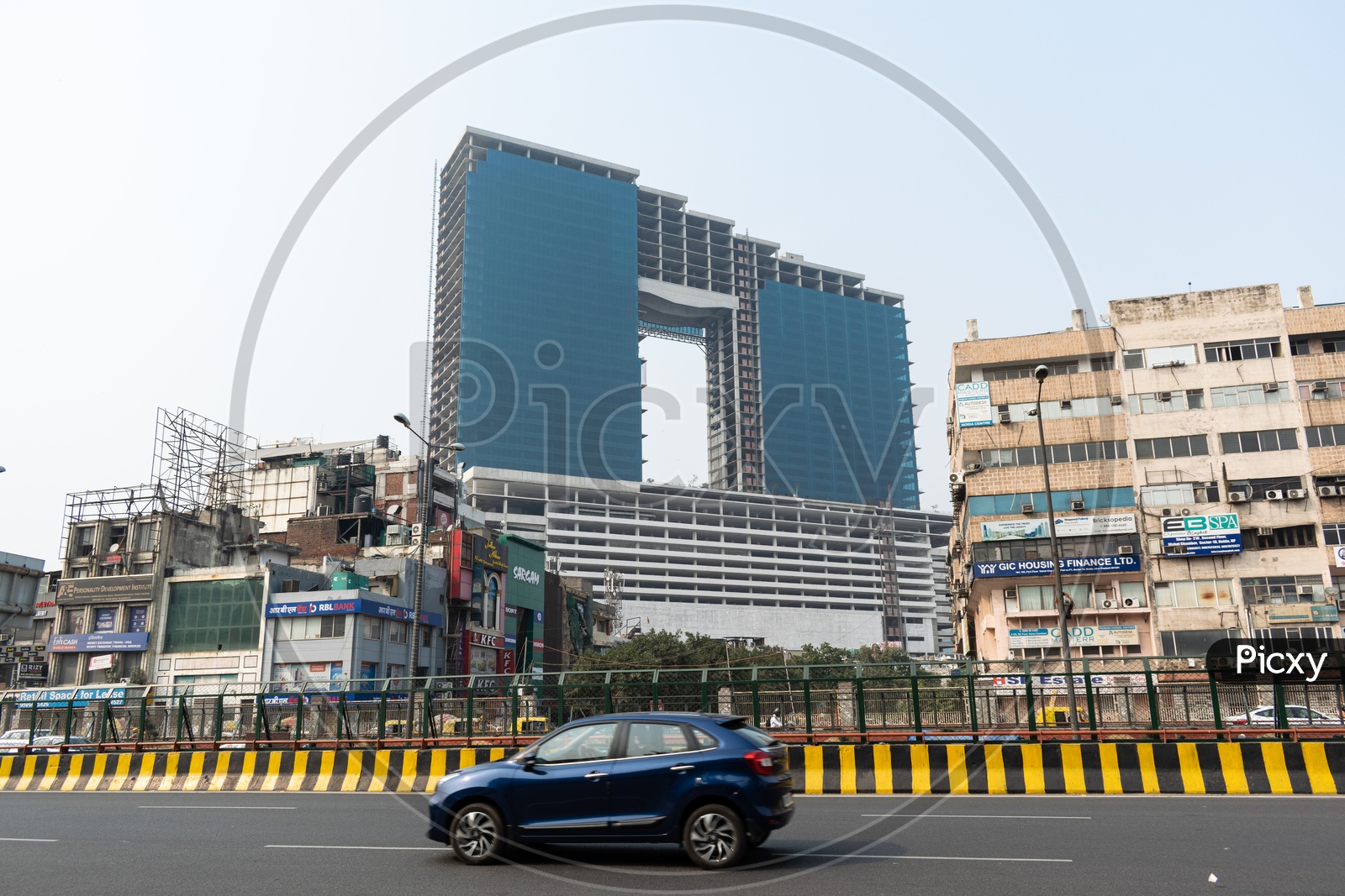 Wave one noida mall construction, other commercial building nearby and a moving car