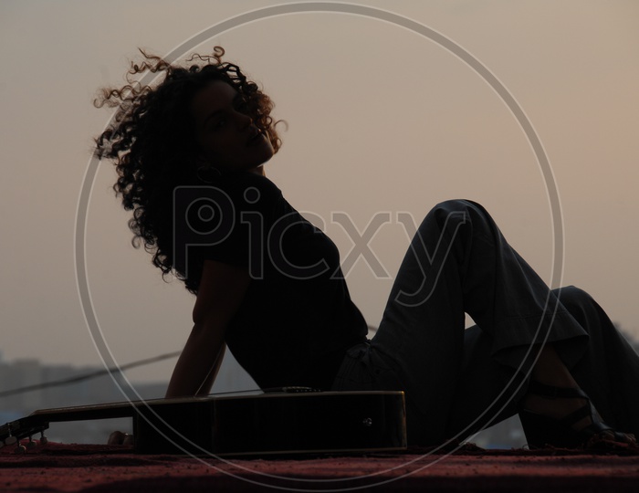 Silhouette Of Woman Enjoying Evening Light With a Guitar Besides Her