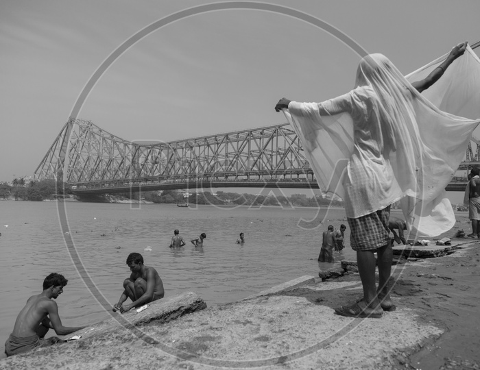 A man stands with his wet cloth draped around in an elegant manner, waiting for it to dry  as other devotees take a dip in the holy Ganges in the background.