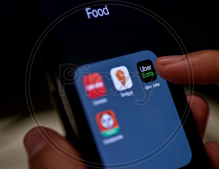 Man Finger Opening An Online Food Ordering Or Delivering App Icons On a Smartphone Screen With Selective Focus on Uber Eats