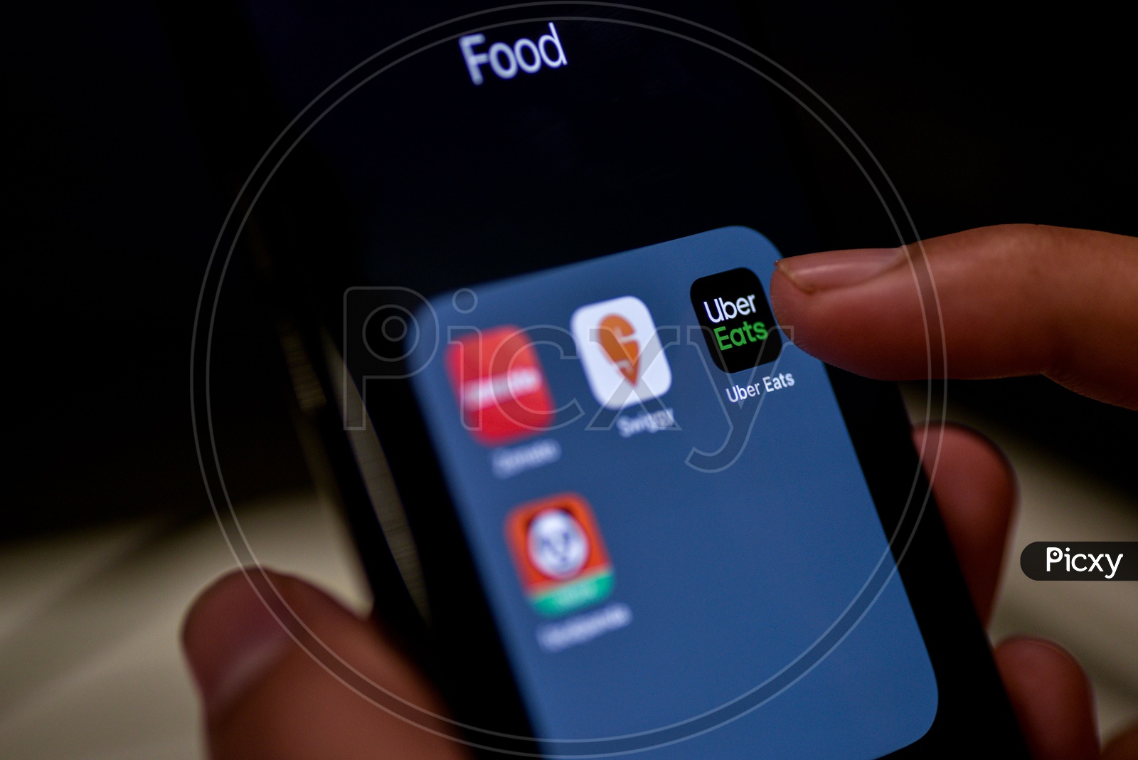 Man Finger Opening An Online Food Ordering Or Delivering App Icons On a Smartphone Screen With Selective Focus on Uber Eats