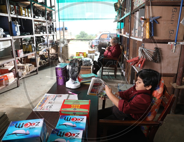 Young Boy Reading Newspaper By Sitting At a Shop Cash Counter