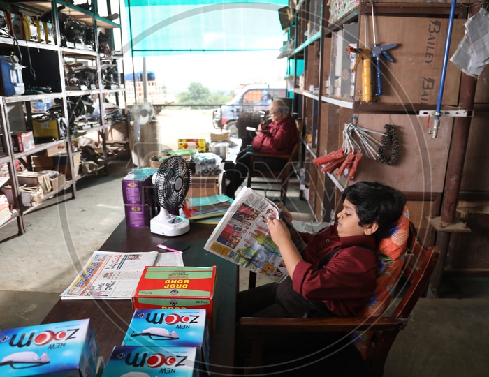Young Boy Reading Newspaper By Sitting At a Shop Cash Counter