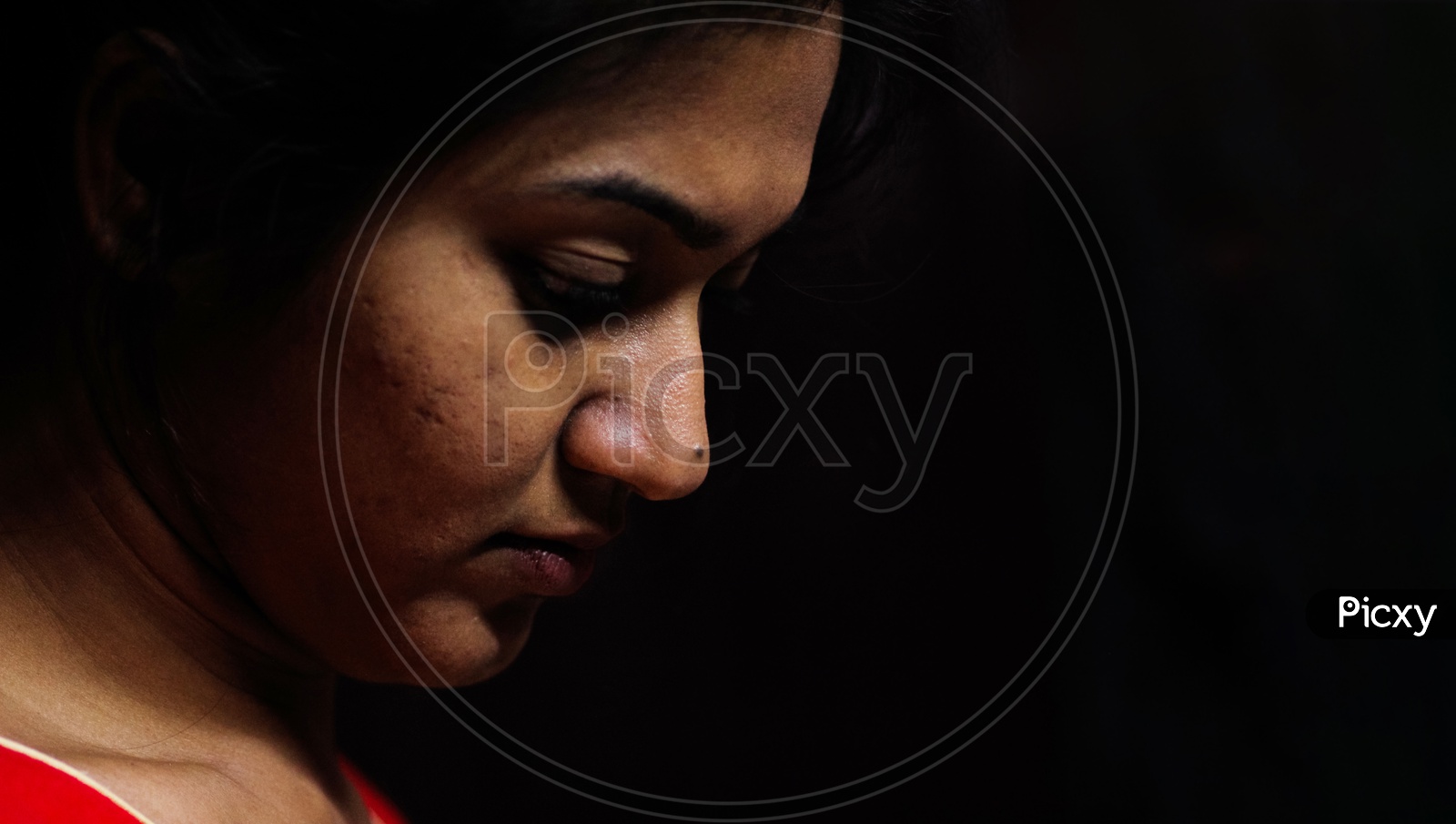 An Indian Female Staring Down In Worry And Depression In Black Background With Selective Focus On Nose