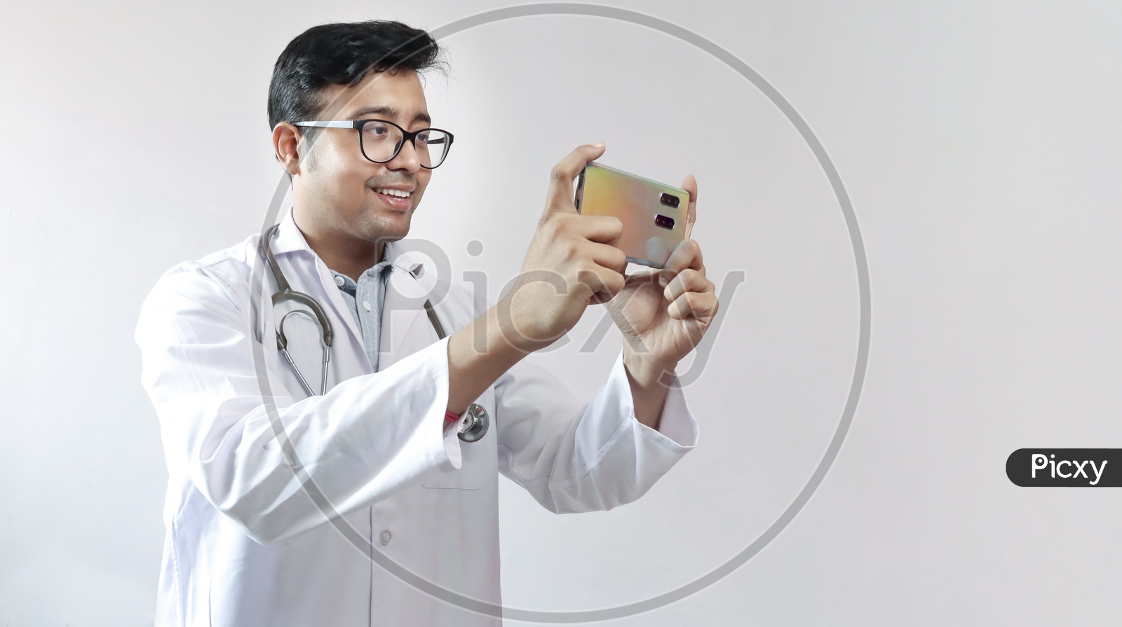 Male Indian Doctor In White Coat And Stethoscope Clicking Photo With A Mobile Tripod And Futuristic Concept Cameraphone