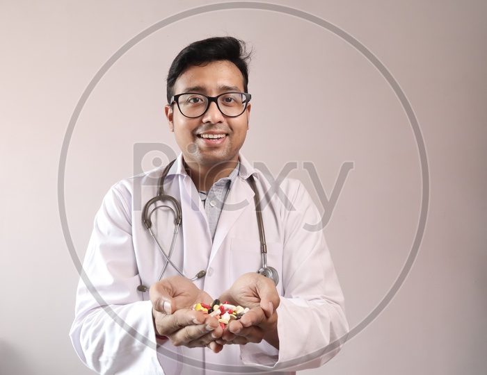 Male Indian Doctor In White Coat And Stethoscope With Medicine Pills Tablets Capsules In Hand