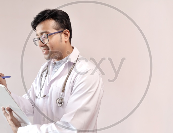 Male Indian Doctor In White Coat And Stethoscope Writing Notes And Prescribing Medicine