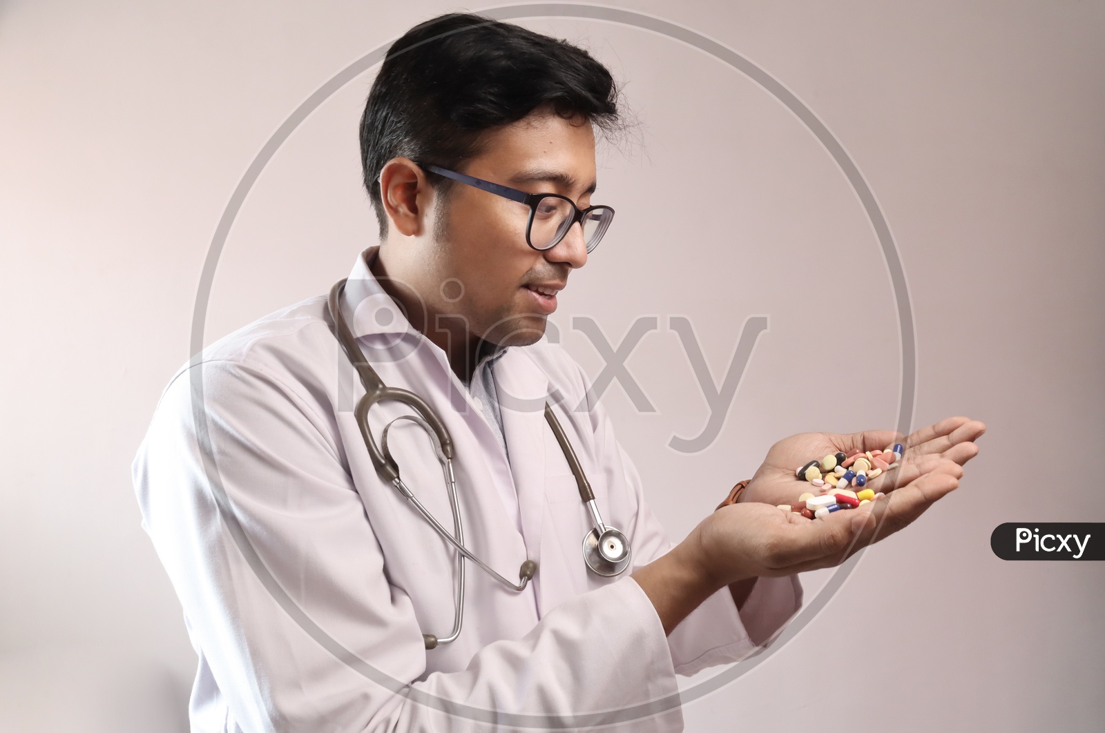 Male Indian Doctor In White Coat And Stethoscope With Medicine Pills Tablets Capsules In Hand