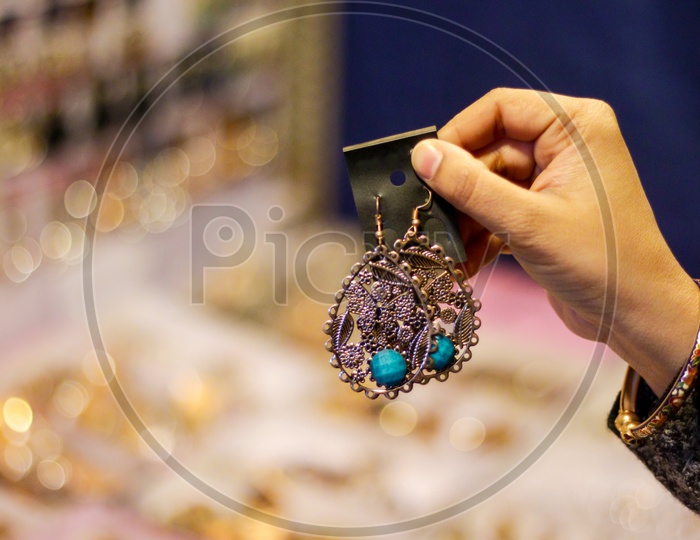 Hand Of A Lady Selecting Ear Rings Metal Junk Jewellery At A Shop.