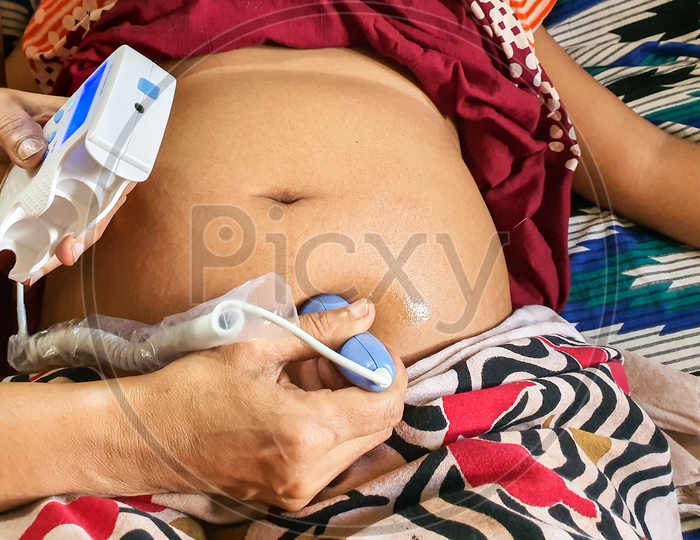 Listening To Fetal Heart Sound On A Pregnant Woman Belly By A Fetal Doppler Machine By A Trained Female Health Worker At Indian Home