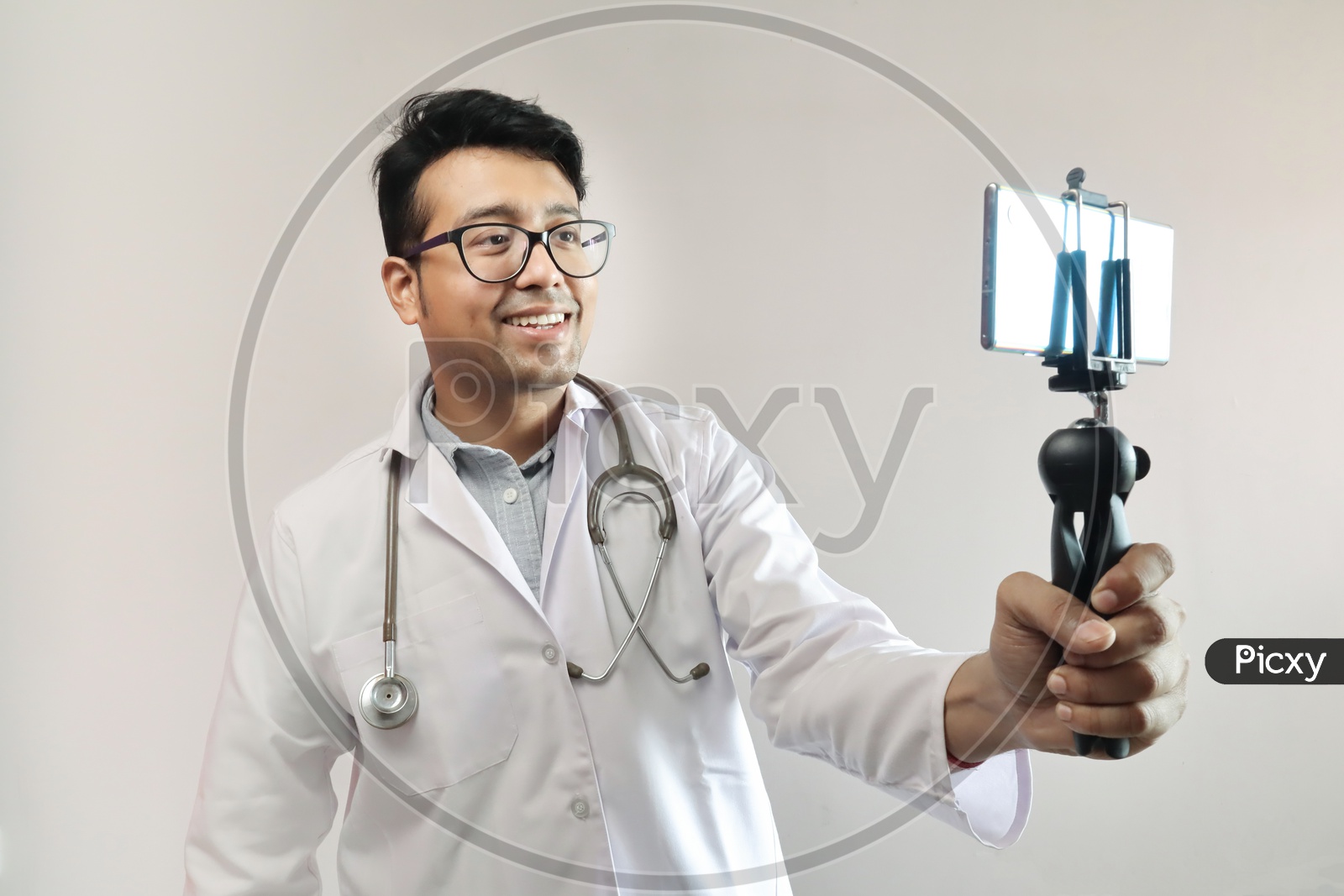 Male Indian Doctor In White Coat And Stethoscope Clicking Selfie With A Mobile Tripod And Futuristic Concept Cameraphone