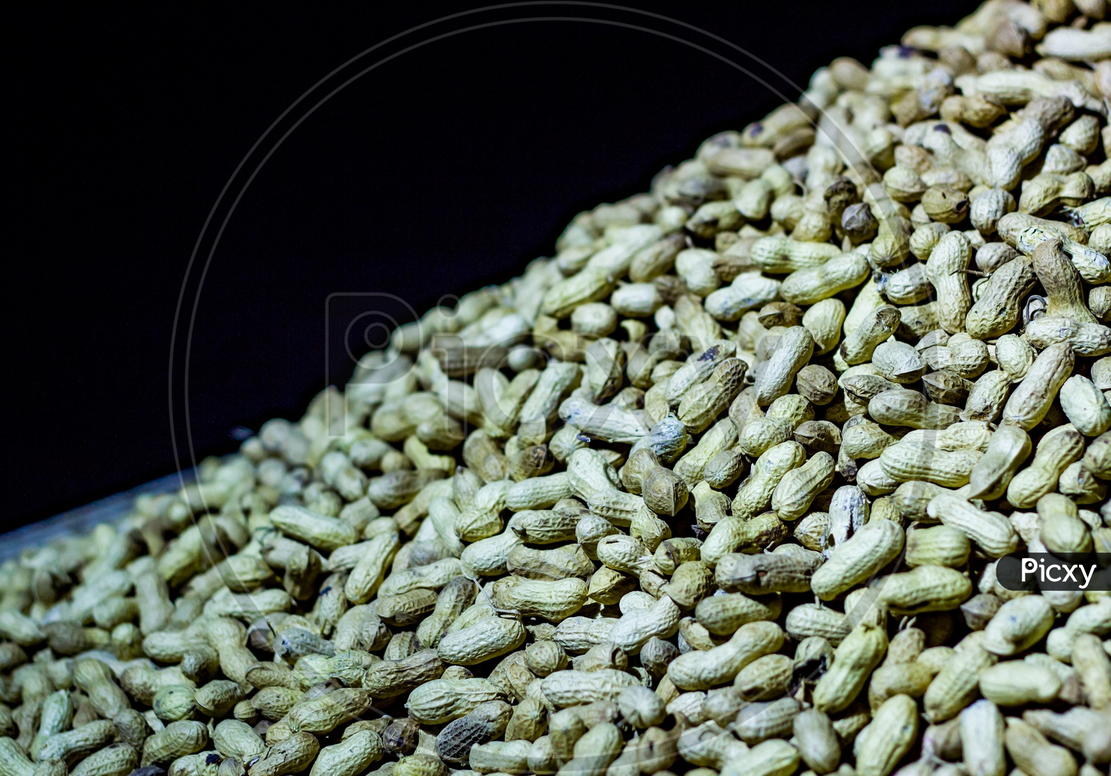 Ground Nuts In A Heap For Sale Against Black Background. Peanut With Shell.