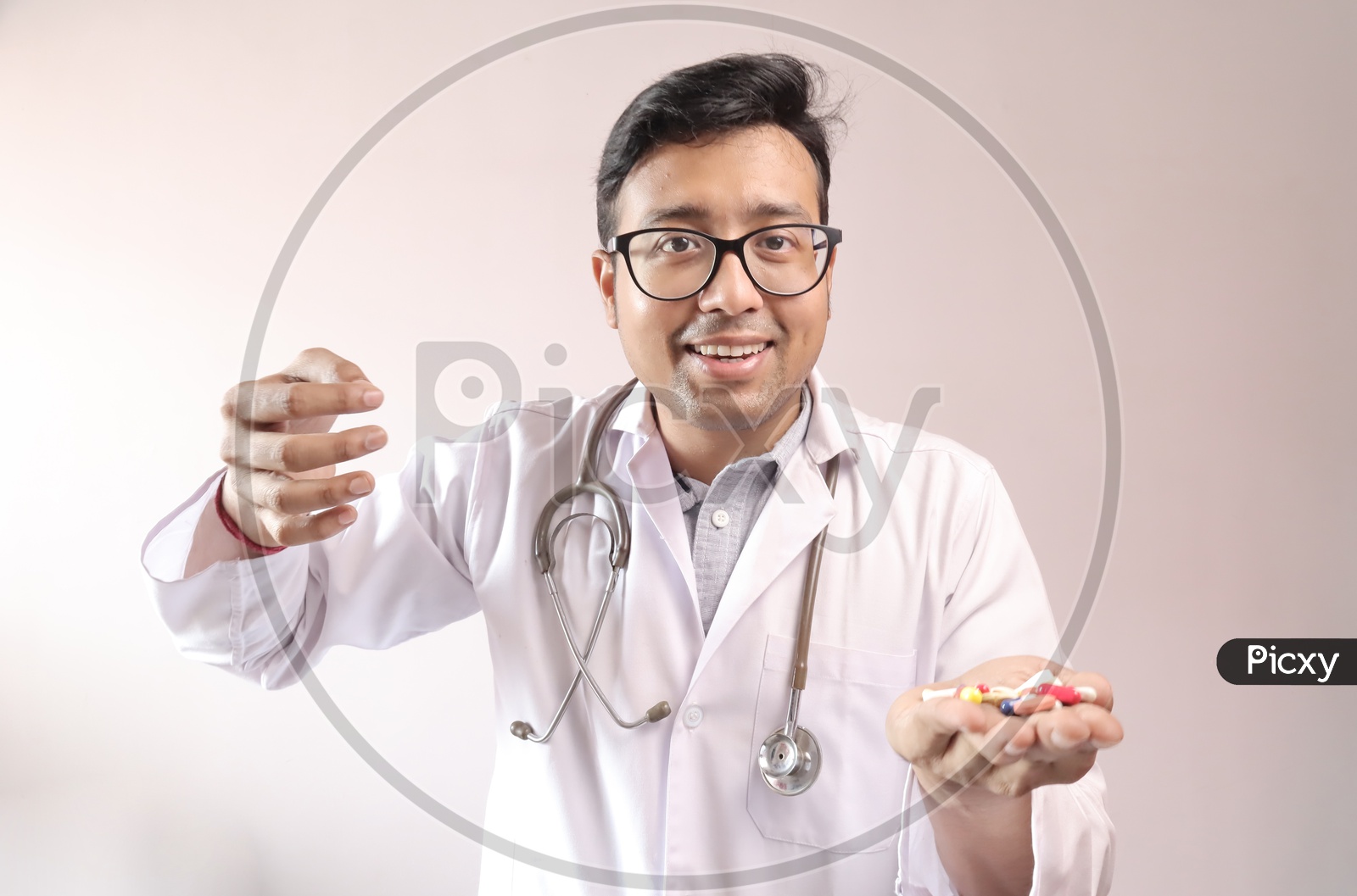Male Indian Doctor In White Coat And Stethoscope With Medicine Pills Tablets Capsules In Hand And Showing Money Sign
