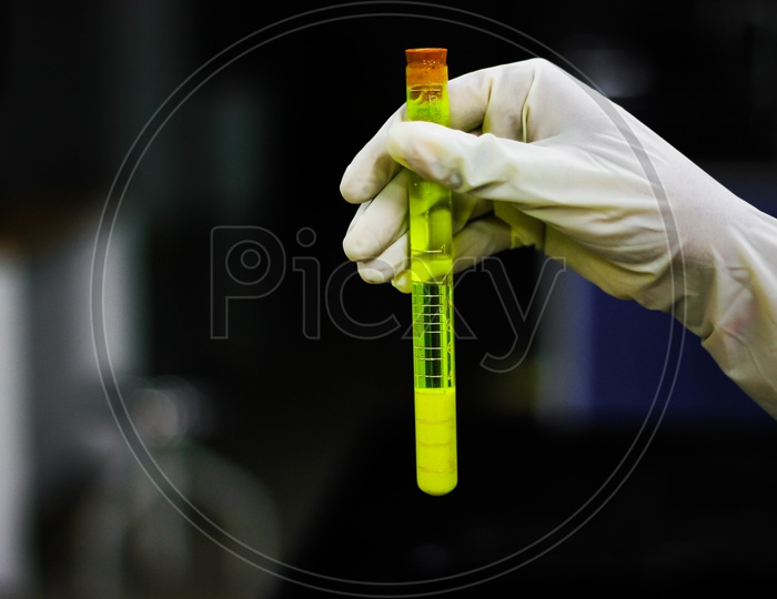 Scientist Holding Albuminometer Containing Yellow Solution With A Cork A Gloved Hand In Chemistry Laboratory