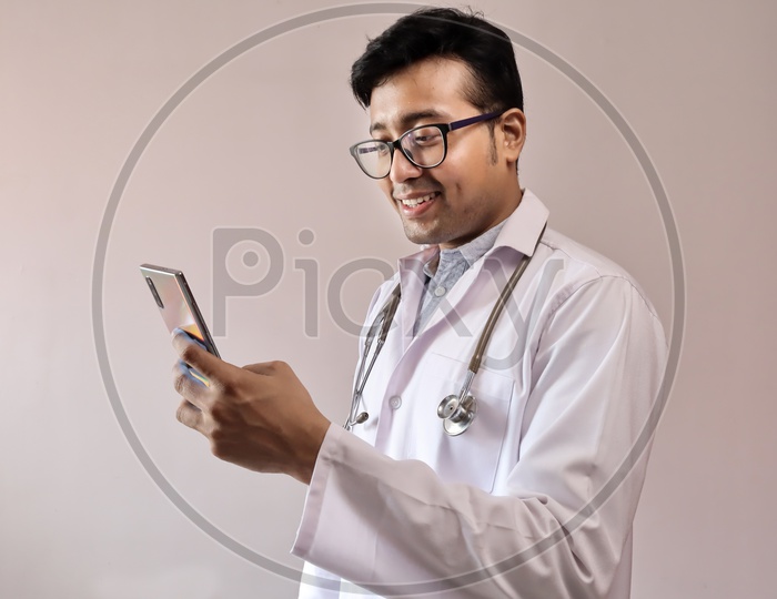 Male Indian Doctor In White Coat And Stethoscope using Smart Phone or Mobile