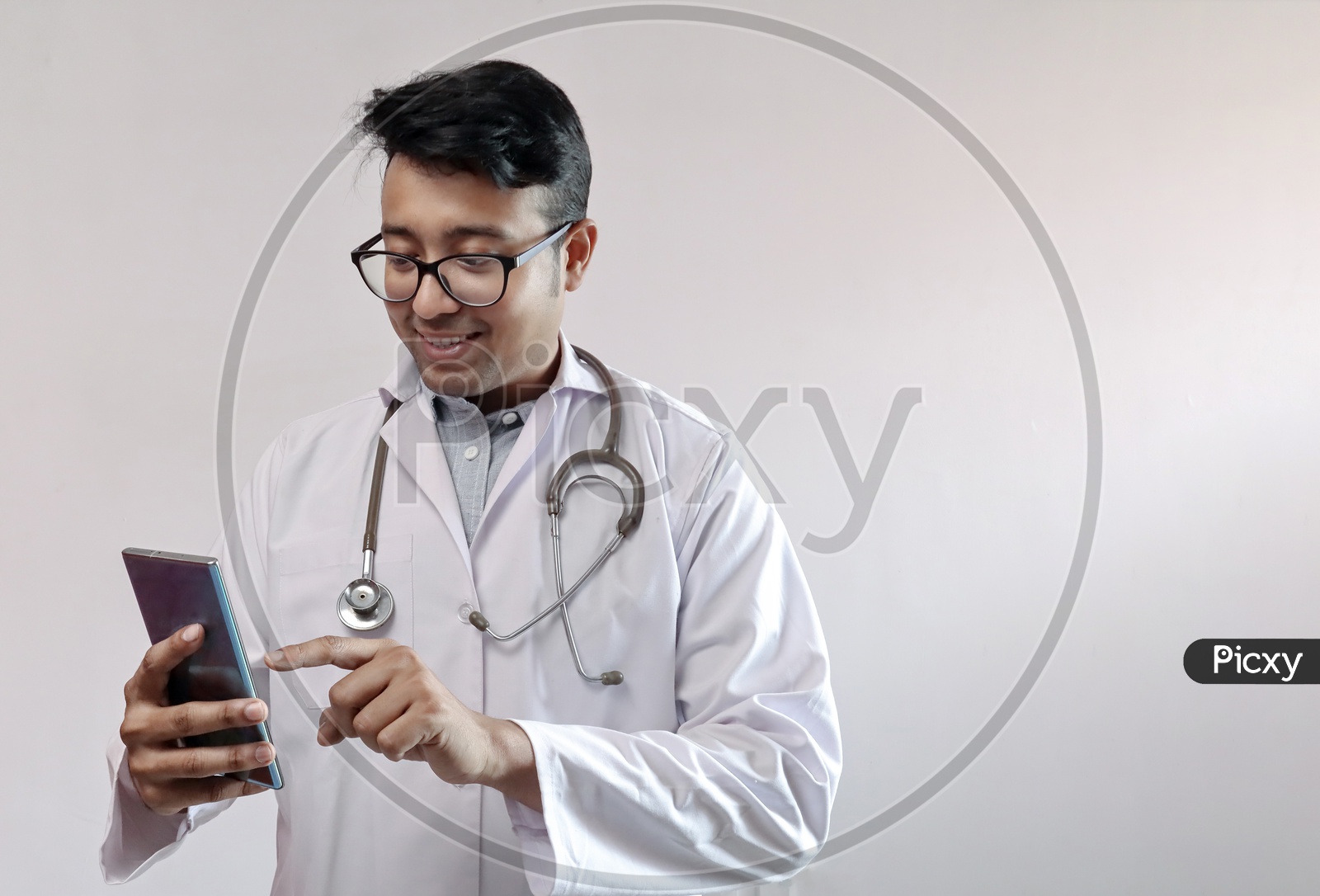Male Indian Doctor In White Coat And Stethoscope Touching Smart Phone or Mobile