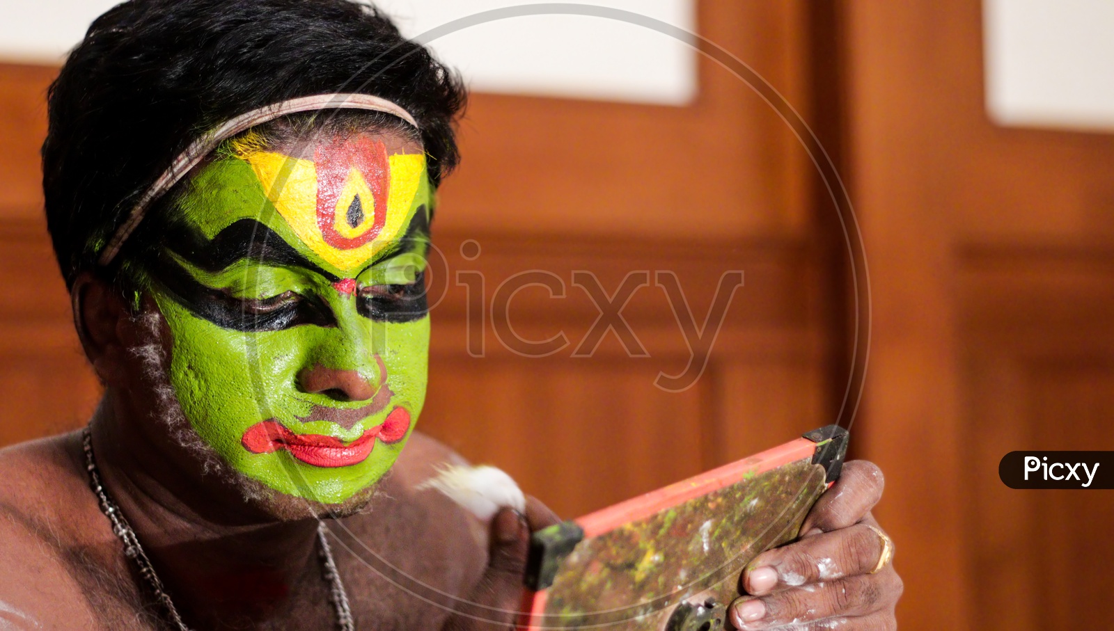 Kathakali dance performer doing face paint and makeup in front of hand held mirror