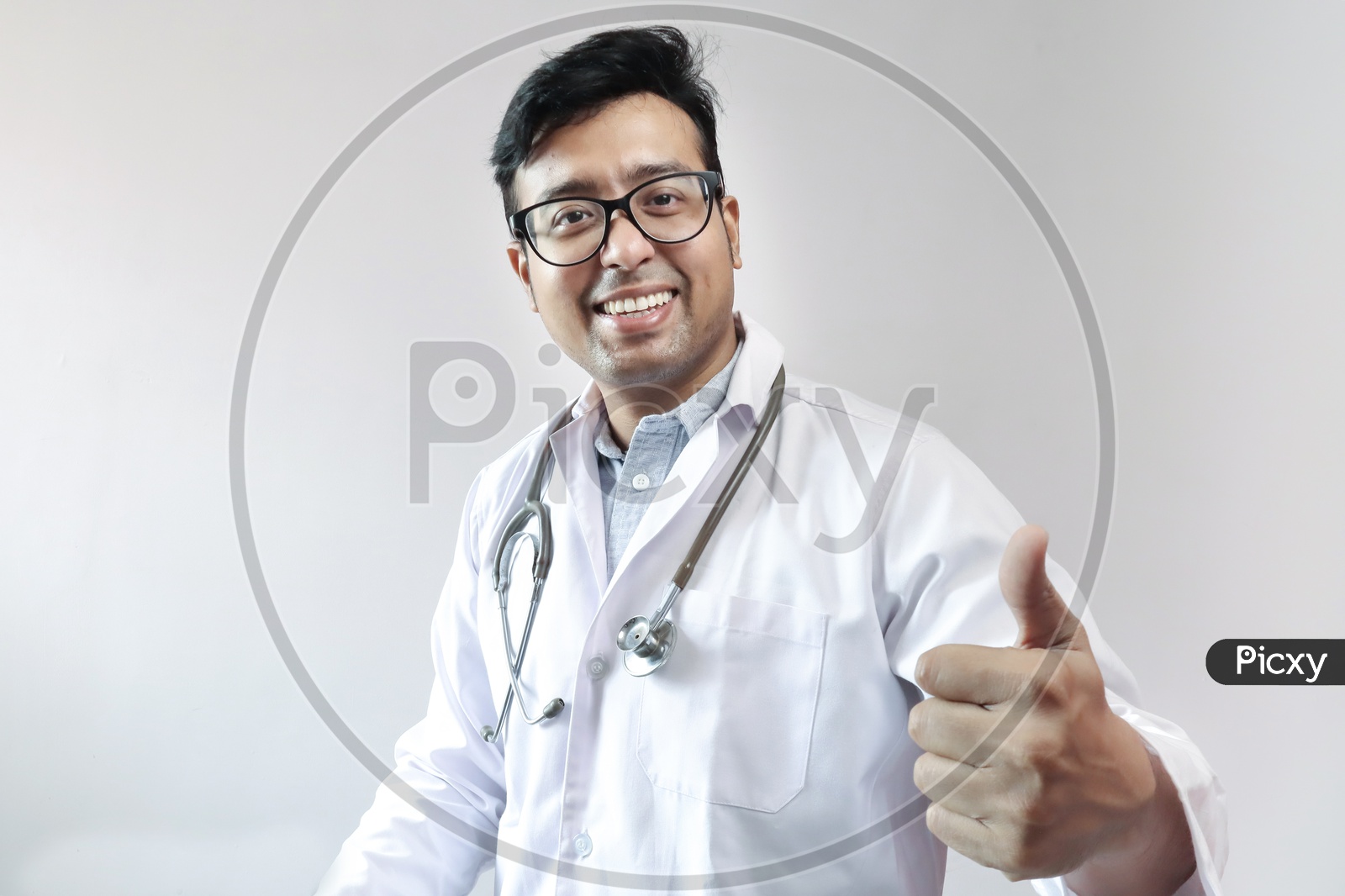 Male Indian Doctor In White Coat And Stethoscope Showing Thumbs Up With Smart Phone