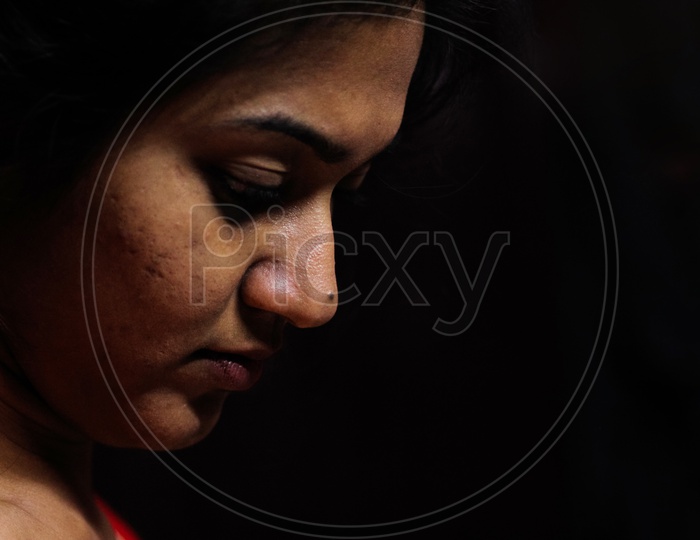 An Indian Female Staring Down In Worry And Depression In Black Background With Selective Focus On Nose