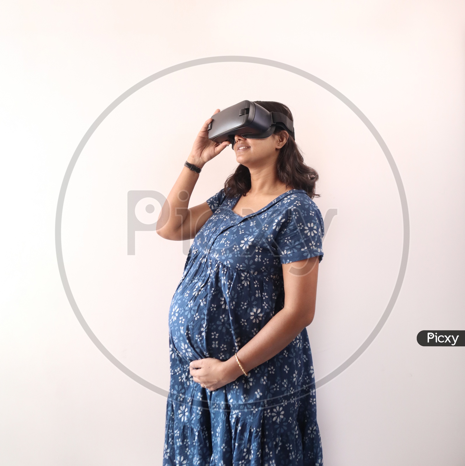 A Pregnant Woman With Hands On Belly And using Virtual Reality Glass In Eye In Blue Dress.