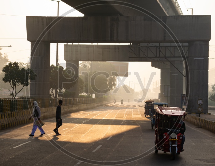 Metro line passing over a road and vehicles and people in a foggy morning