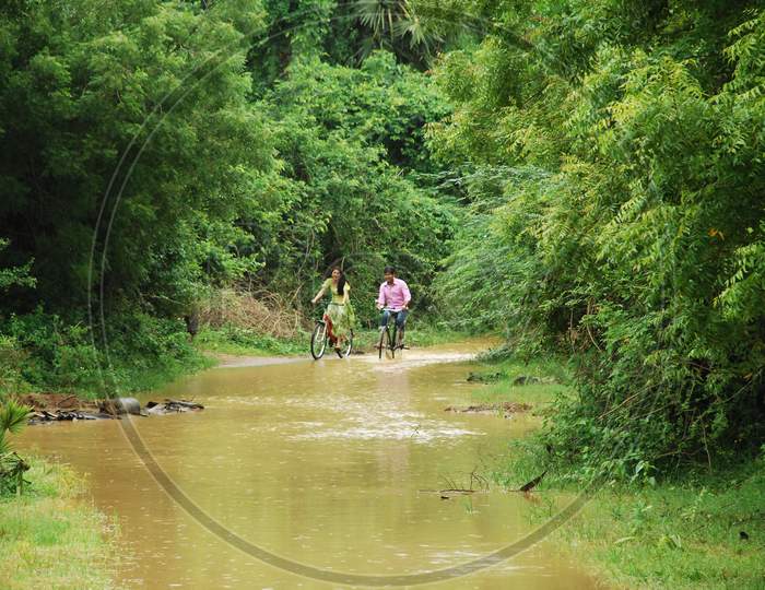 A Couple  Riding Bicycle In an Forest Lane With Water Channel
