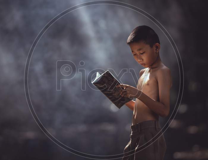 Little Asian Boy Reading A Book Outdoors In Rural Areas