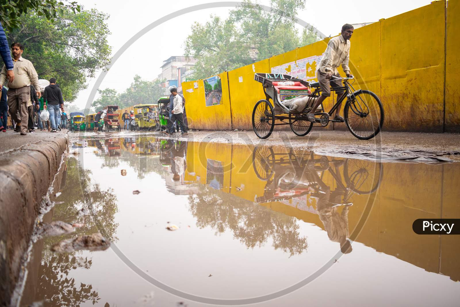 a rickshaw wala riding the rickshaw near the road filled with rain water