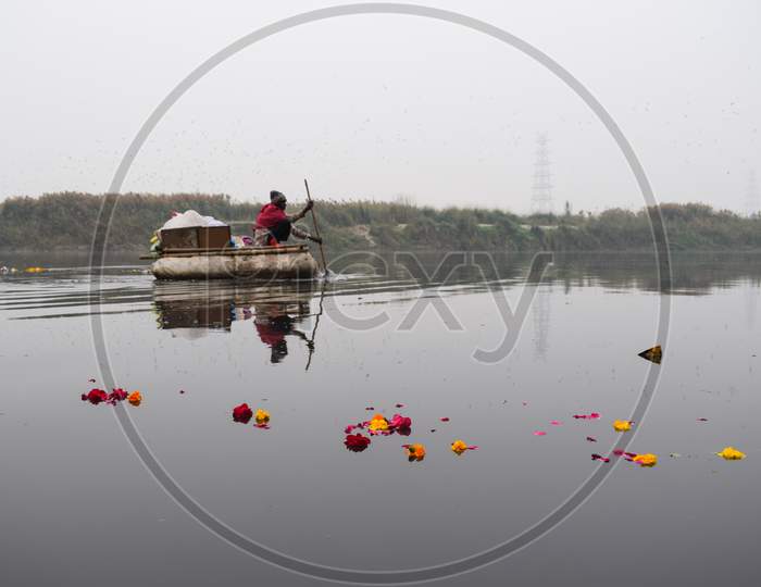 A man rowing boat and immersing flowers in Yamuna river near Yamuna Ghat in Delhi