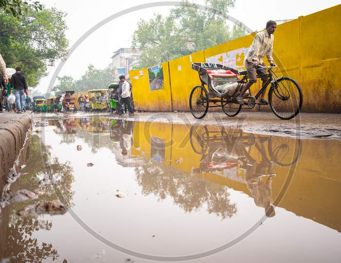 a rickshaw wala riding the rickshaw near the road filled with rain water