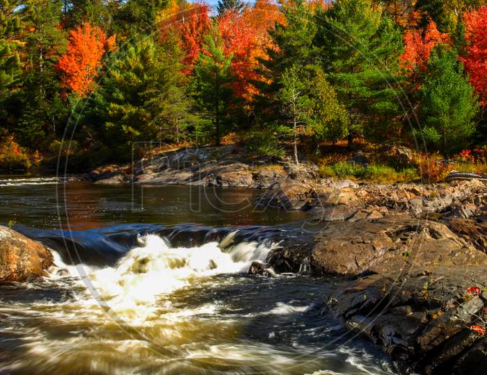 Bright sky, clouds, and fall foliage add to the flowing river, Chutes Prov Park, ON, Canada
